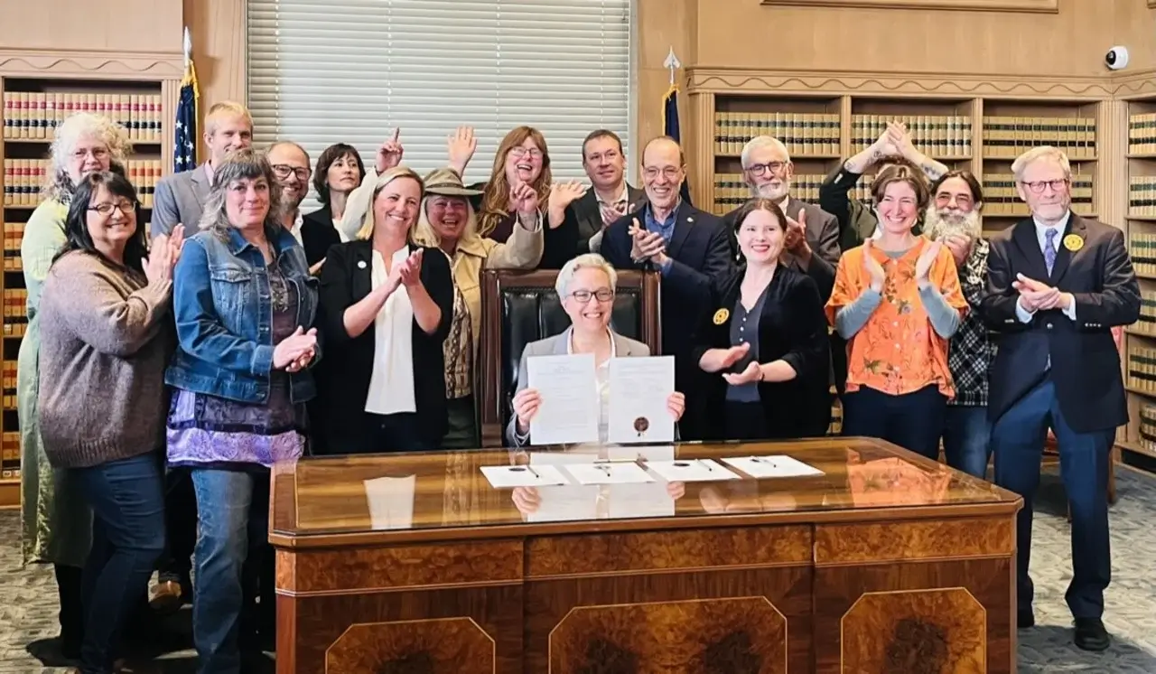 A group of people stand while Oregon's governor signs a bill into law.